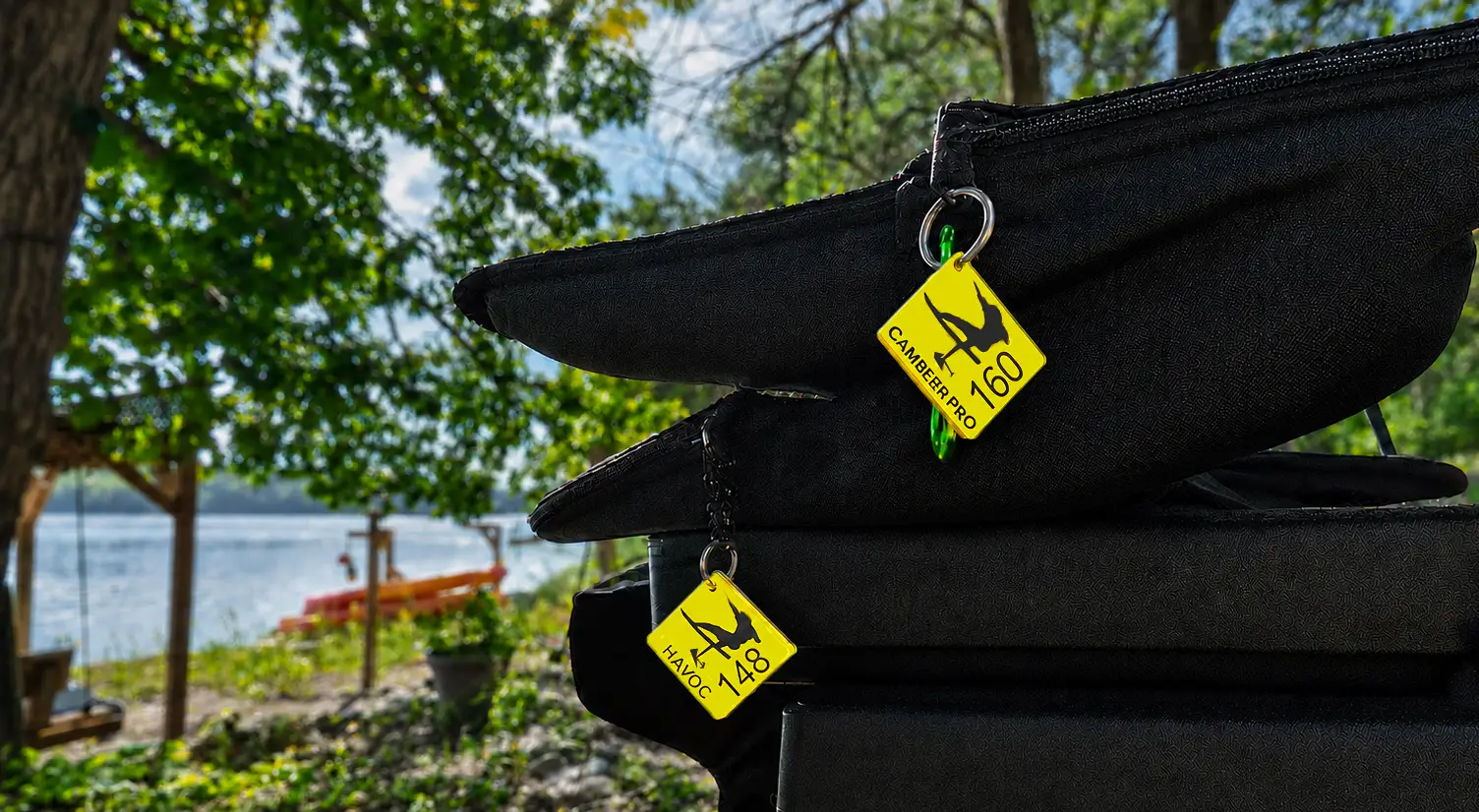 Two yellow 3D printed eFoil gear tags hanging from the zippers of stacked black Lift wing bags, lake in the background