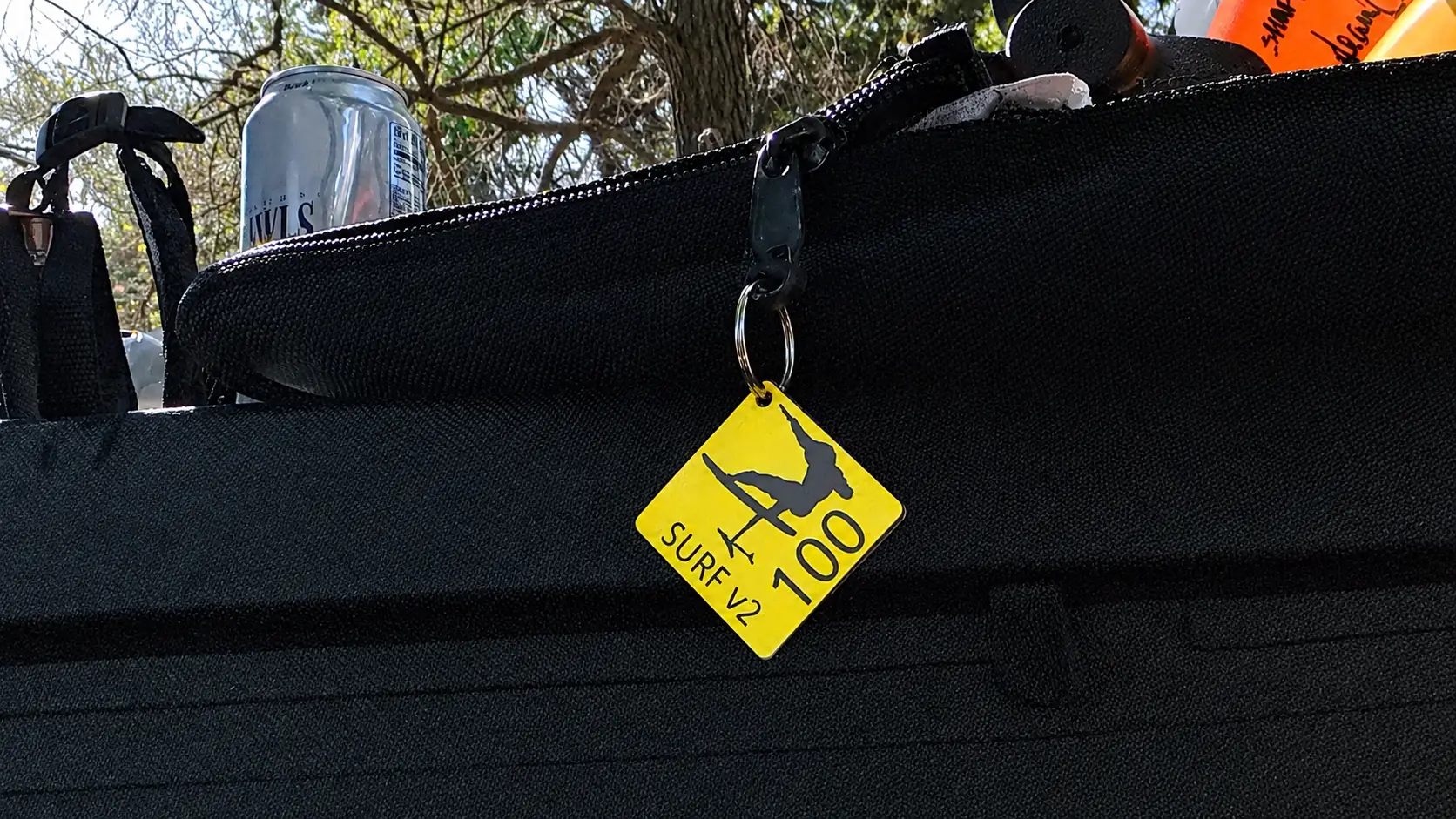 Yellow 3D printed eFoil gear tag reading SURF V2 100 clipped to the zipper pull of a black wing bag