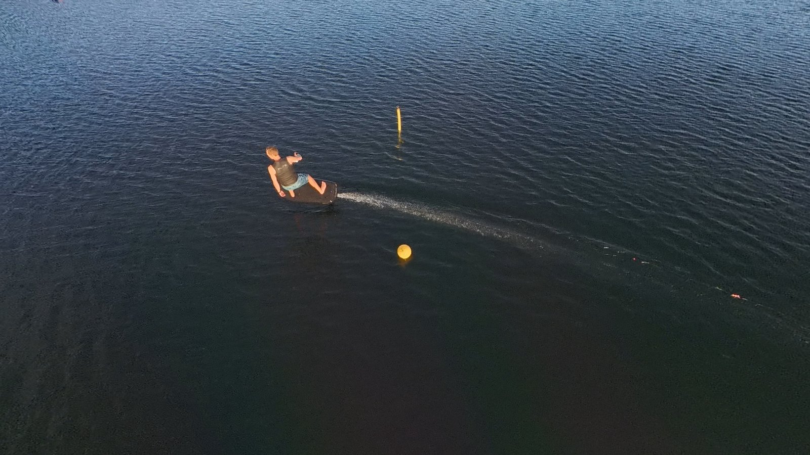 An eFoil rider leaning into a carve past a yellow race buoy on a dark lake