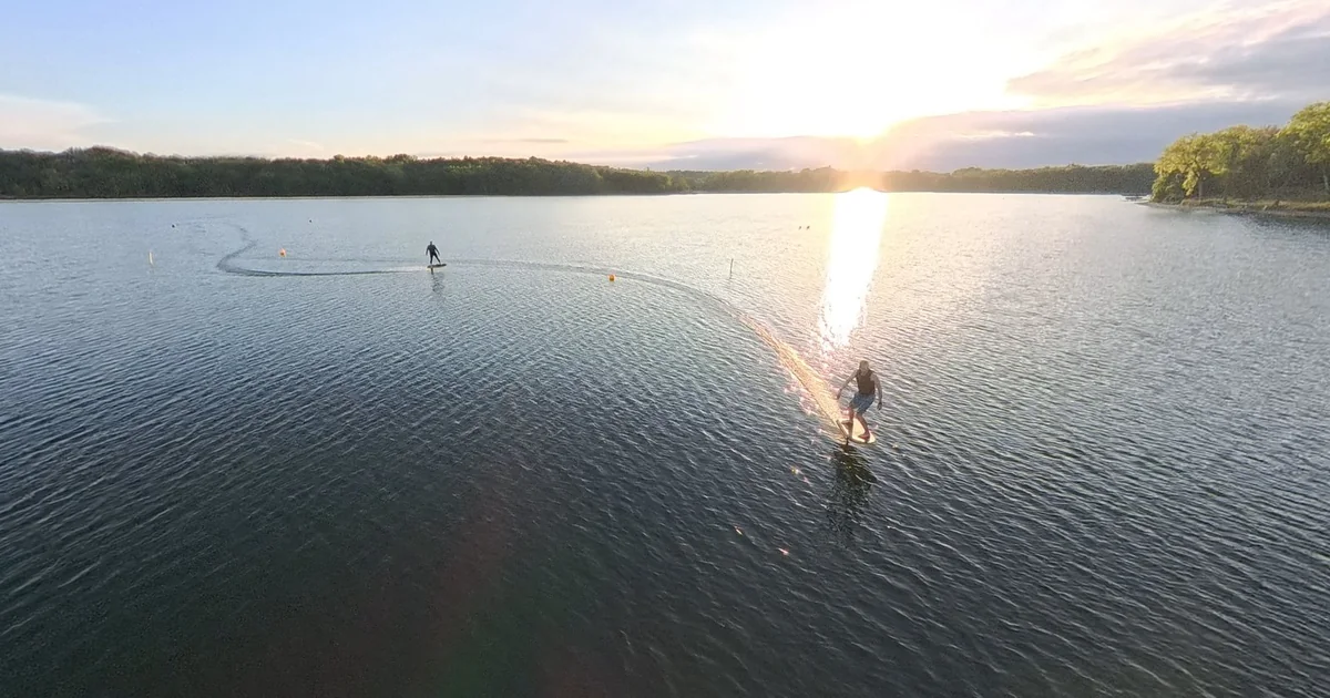 Two eFoil riders carving long arcs across a calm lake at sunset between race buoys